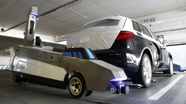 Automated guided vehicle robot “Ray” lifts up an Audi car during a pilot project at the parking area of the Audi plant in Ingolstadt, Germany, May 13, 2015. The robot has been designed to help make work more efficient and more comfortable for employees, some whom walk up to eight kilometres a day, while coordinating the finished cars for the subsequent train transportation. (Photo by Michaela Rehle/Reuters)