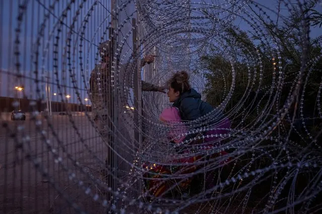Eliana, 22, a migrant from Venezuela, holds her three-year-old daughter Chrismarlees as she shouts towards an Army National Guard soldier after he halts her from breaching a razor wire-laden fence along the bank of the Rio Grande river in El Paso, Texas, U.S., March 26, 2024. Eliana's six-year-old daughter Ariana was carried past the fence by other migrants, who had used wire cutters to breach the razor wire. (Photo by Adrees Latif/Reuters)