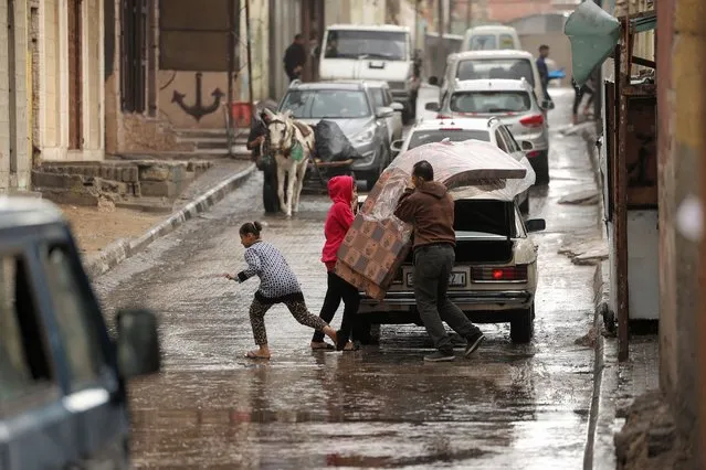 A man is assisted by children as he unloads mattresses from the back of a vehicle during rainy weather at al-Shati camp for Palestinian refugees in Gaza City on November 20, 2021. (Photo by Mahmud Hams/AFP Photo)
