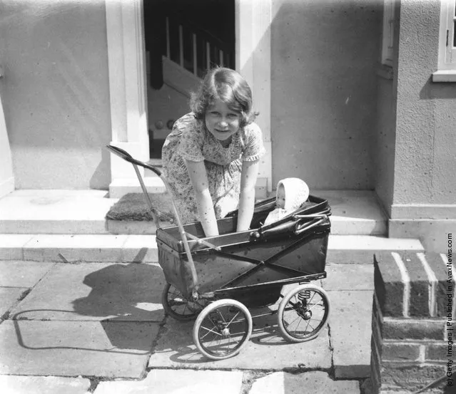 1933: Princess Elizabeth playing with a doll in a toy pram outside the Welsh House, a miniature house presented to Princess Elizabeth and Princess Margaret by the people of Wales in the grounds of the Royal Lodge, Windsor