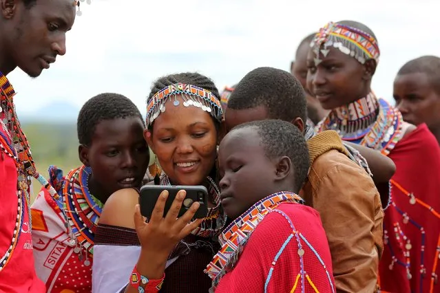 Maasai girls and a man watch a video on a mobile phone prior to the start of a social event advocating against harmful practices such as Female Genital Mutilation (FGM) at the Imbirikani Girls High School in Imbirikani, Kenya, April 21, 2016. (Photo by Siegfried Modola/Reuters)