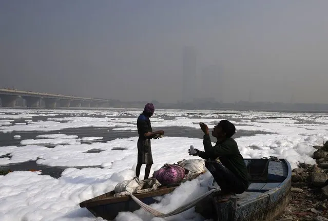 A person eats snack sitting on his boat in the Yamuna River, covered by a chemical foam caused by industrial and domestic pollution as the skyline is enveloped in a blanket of toxic smog,  in New Delhi, India, Wednesday, November 17, 2021. Schools were closed indefinitely and some coal-based power plants shut down as the Indian capital and neighboring states invoked harsh measures Wednesday to combat air pollution after an order from the federal environment ministry panel. (Photo by Manish Swarup/AP Photo)