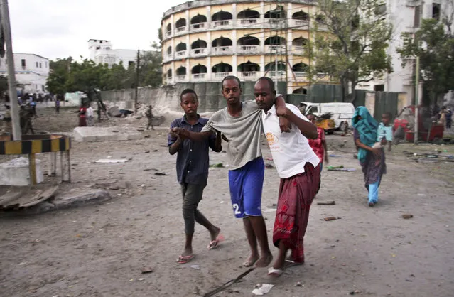 An injured man is assisted after a suicide car bomb attack that targeted a check point in Mogadishu, Somalia, Tuesday, March 21, 2017. The car bomb exploded Tuesday at a military checkpoint near Somalia's presidential palace in the capital after soldiers tried to stop the car and the bomber tried to speed through the checkpoint, killing a number of people, police said. (Photo by Farah Abdi Warsameh/AP Photo)
