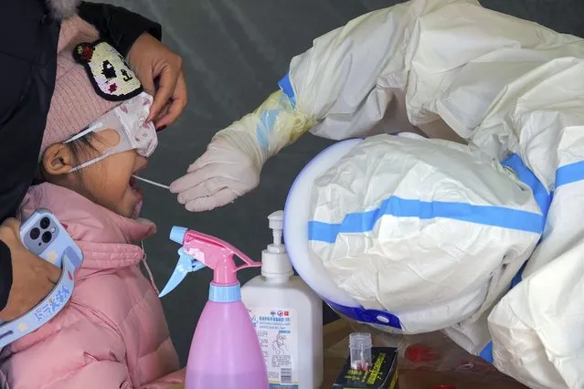 A medical worker takes swab samples from a girl for the Covid-19 screening in Yantai city in eastern China's Shandong province Monday, March 14, 2022. China banned most people from leaving a coronavirus-hit northeastern province and mobilized military reservists Monday as the fast-spreading “stealth omicron” variant fuels the country's biggest outbreak since the start of the pandemic two years ago. (Photo by Chinatopix via AP Photo)