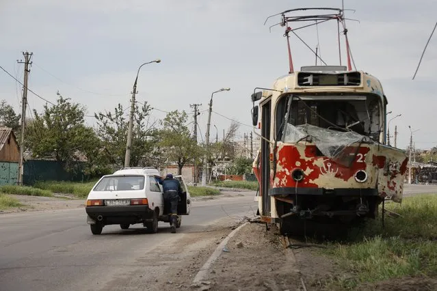A man pushes a stalled car past a damaged tram in Mariupol, in territory under the government of the Donetsk People's Republic, eastern Ukraine, Saturday, May 21, 2022. (Photo by Alexei Alexandrov/AP Photo)