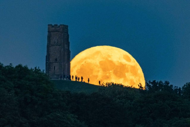 The full Strawberry moon rises up from behind St Michael's Tower on Glastonbury Tor in Somerset, United Kingdom on June 3, 2023 as a crowd of people gather on top of the hill to watch. (Photo by Graham Hunt/Alamy Live News)