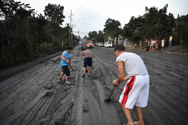 Residents help scrape a road covered wih mud spewed by Taal volcano over Tanauan town, Batangas province south of Manila on January 13, 2020. Lava and broad columns of ash illuminated by lightning shot from an erupting volcano south of the Philippine capital on January 13, grounding hundreds of flights amid an alert for a possible “explosive eruption”. (Photo by Ted Aljibe/AFP Photo)