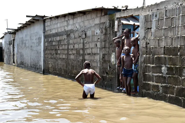 Young boys stand in a street flooded by rain water in the impoverished neighborhood of Adjouffou in Abidjan, Ivory Coast, on July 9, 2014. Several weeks of torrential rainfall in the Ivorian economic capital have left several people dead and caused substantial damage to the city and other areas of the country. (Photo by Issouf Sanogo/AFP Photo)