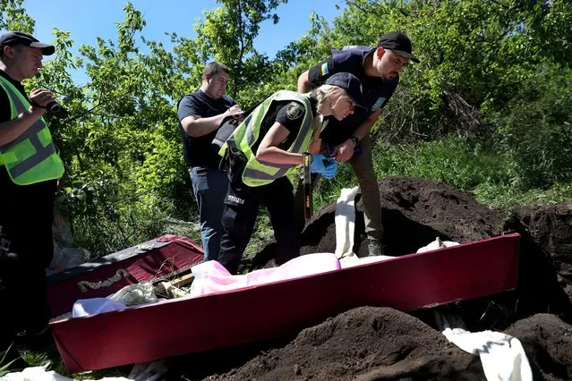Prosecutor's office members inspect the body of Inna Bobryntseva, who died during a Russian shelling, in the backyard of her house, during an exhumation as part of a prosecutor's investigation into war crime cases on the outskirt of Kharkiv, Ukraine on June 6, 2022. (Photo by Ivan Alvarado/Reuters)