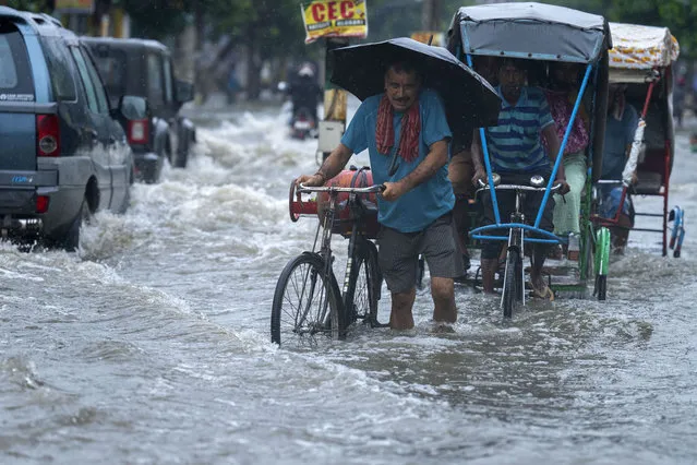 A man carries a gas cylinder on his bicycle and wades through a flooded street during heavy rainfall in Gauhati, India, Thursday, June 16, 2022. (Photo by Anupam Nath/AP Photo)