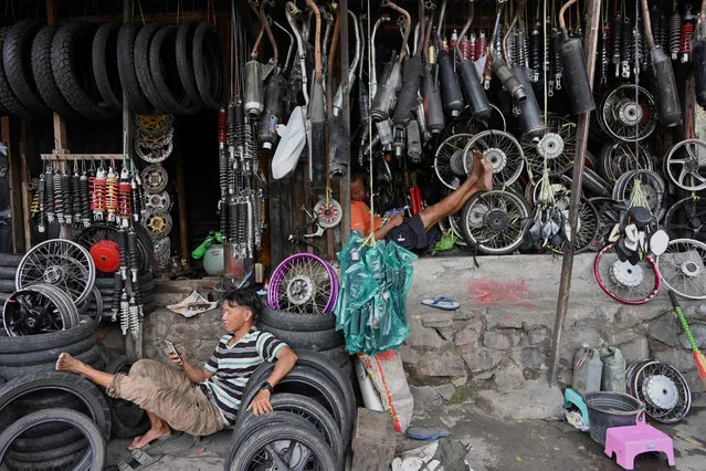 Two men wait for customers at their motorcycle repair workshops in Jakarta on March 11, 2020. (Photo by Adek Berry/AFP Photo)