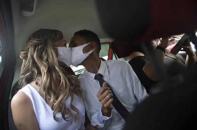 Wearing masks to prevent the spread of the new coronavirus, Thiago do Nascimento, right, and Keilla de Almeida kiss during their drive-thru wedding at the registry office in the neighborhood of Santa Cruz, Rio de Janeiro, Brazil, Thursday, May 28, 2020. Couples have begun turning to this unconventional union at a notary in Santa Cruz since the COVID-19 started battering Brazil. (Photo by Silvia Izquierdo/AP Photo)