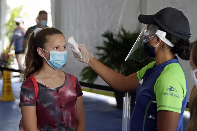 A guest has her temperature checked before entering SeaWorld as it reopens with new safety measures in place because of the coronavirus pandemic, Thursday, June 11, 2020, in Orlando, Fla. The park had been closed since mid-March to stop the spread of the new coronavirus. (Photo by John Raoux/AP Photo)
