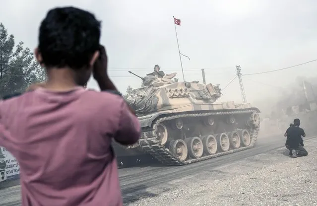 A boy looks at Turkish army tanks and armored personnel carriers moving toward the Syrian border, in Karkamis, Turkey, Thursday, August 25, 2016. Turkish President Recep Tayyip Erdogan late Wednesday said that Syrian opposition forces aided by Ankara have taken back the border town of Jarablus from the Islamic State group. Erdogan said the Syrian rebels, “together with those who are from Jarablus, have now taken it back and IS has been forced to leave Jarablus”. (Photo by Halit Onur Sandal/AP Photo)