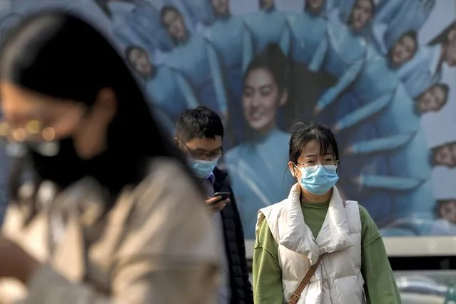 People wearing face masks walk by an advertisement billboard on street in Beijing, Wednesday, November 2, 2022. (Photo by Andy Wong/AP Photo)