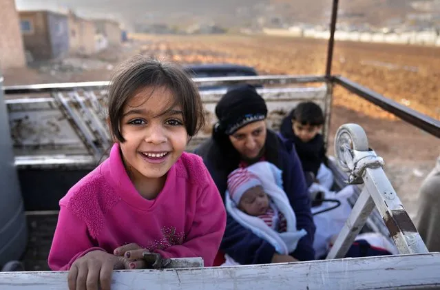 A Syrian refugee girl stands on a pickup next to her mother, as they wait at a gathering point to cross the border back home to Syria, in the eastern Lebanese border town of Arsal, Lebanon, Wednesday, October 26, 2022. Several hundred Syrian refugees boarded a convoy of trucks laden with mattresses, water and fuel tanks, bicycles – and, in one case, a goat – Wednesday morning in the remote Lebanese mountain town of Arsal in preparation to return back across the nearby border.(Photo by Hussein Malla/AP Photo)