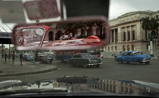 In this October 16, 2014 photo, people drive classic American car in Old Havana, Cuba. These classic cars are now part of Havana's tourist draw. That's allowed many to paint and polish their aging vehicles. (Photo by Franklin Reyes/AP Photo)
