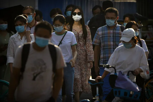 People wearing face masks to protect against the coronavirus wait to cross an intersection in the central business district in Beijing, Wednesday, July 15, 2020. China is further easing restrictions on domestic tourism after reporting no new local cases of COVID-19 in nine days. (Photo by Mark Schiefelbein/AP Photo)