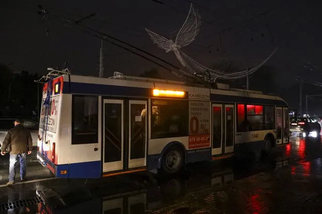 A man walks by a trolley bus that is stuck on a boulevard during a power outage in Chisinau, Moldova, Wednesday, November 23, 2022. Moldova suffered massive power outages on Wednesday after Russian strikes on neighboring Ukraine's energy infrastructure left the small non-European Union country in the dark for the second time in little more than a week. (Photo by Aurel Obreja/AP Photo)