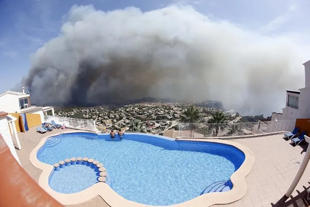 Two men look at a wildfire from a swimming pool as it burns nearby Benitachel village, eastern Spain, Monday, September 5, 2016. Spanish firefighters are still working to bring under control a forest blaze near Valencia that forced the evacuation of around 1,000 people. Authorities said more than 200 firefighters with 65 vehicles were deployed Monday to the wildfire some 350 kilometers (220 miles) southeast of Madrid. (Photo by Alberto Saiz/AP Photo)
