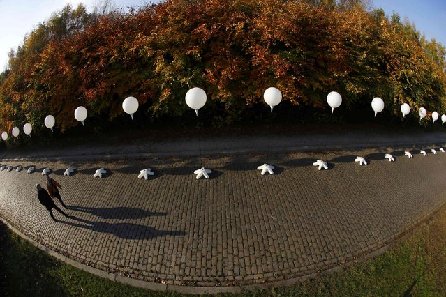 People walk under stands with balloons placed along the former Berlin Wall location at Mauerpark, which will be used in the installation “Lichtgrenze” (Border of Light) in Berlin November 7, 2014. A part of the inner city of Berlin will be temporarily divided from November 7 to 9, with a light installation featuring 8000 luminous white balloons to commemorate the 25th anniversary of the fall of the Berlin Wall. (Photo by Pawel Kopczynski/Reuters)