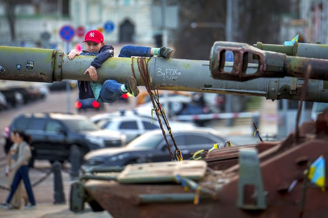 A boy holds on to the barrel of a tank, part of a display of destroyed Russian military equipment, in Kyiv, Ukraine, Sunday, March 31, 2024. (Photo by Vadim Ghirda/AP Photo)