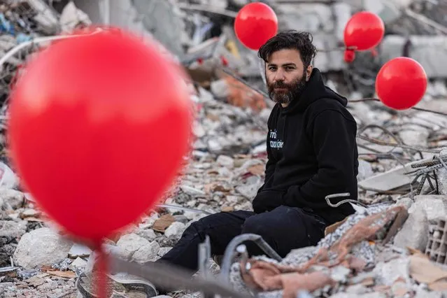 Ogun Sever Okur, 38-year-old Turkish man poses among ballons hanging on the debris of a collapsed building in Antakya, southern Turkey on February 21, 2023, following the 6.4-magnitude earthquake which struck on February 20, two weeks after a 7.8-magnitude earthquake hit near Gaziantep and has killed more than 44,000 people. On the side of a busy road in Antakya, dozens of red balloons flutter around, hanging from the ruins. They are “the last toys” of children who died during the earthquake that devastated this southern Turkish city, explains Ogun Sever Okur, the author of this posthumous gift. (Photo by SAmeer Al-Doumy/AFP Phoot)