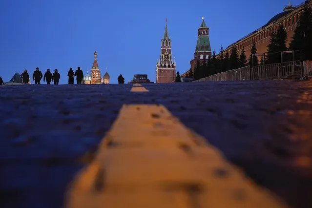 People walk in Red Square with St. Basil's Cathedral, left, Lenin's Mausoleum, center, the Spasskaya Tower and the Kremlin Wall, right, after sunset in Moscow, Russia, Monday, March 13, 2023. (Photo by Alexander Zemlianichenko/AP Photo)