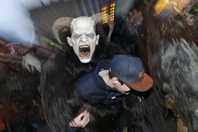 A man dressed as “Krampus” creature takes part in a parade at Munich's Christmas market, December 14, 2014. Young single men will wear the traditional attires known as “Krampus”, consisting of animal skins and masks, with large cow-bells to make loud and frightening noises and parade through the city. They follow 'Saint Nicholas' from house to house in December each year to bring luck to the good and punish the idle. (Photo by Michaela Rehle/Reuters)