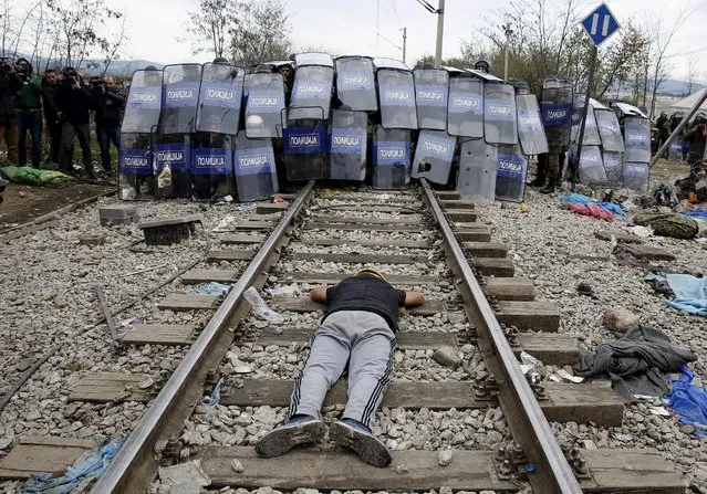 A stranded Iranian migrant lies on the rail tracks in front of a Macedonian police cordon during clashes after a migrant, believed to be a Moroccan, was electrocuted and badly burned when he climbed on top of a train wagon, near the village of Idomeni, Greece, November 28, 2015. (Photo by Yannis Behrakis/Reuters)