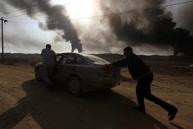 Displaced people push their car as smoke rises from oil wells, set ablaze by Islamic State militants before fleeing the oil-producing region of Qayyara, Iraq, November 4, 2016. (Photo by Alaa Al-Marjani/Reuters)