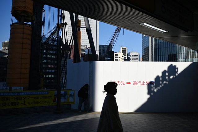 A woman walks past a construction site outside a train station in Tokyo on December 7, 2025. (Photo by Greg Baker/AFP Photo)