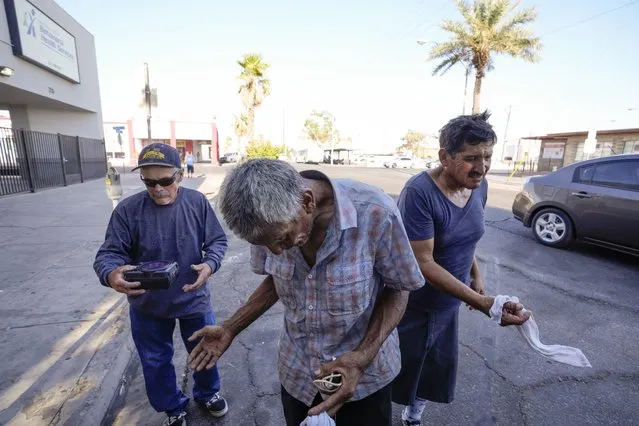 Three men, who are homeless, react as they are given cold, wet towels by Maribel Padilla of the Brown Bag Coalition, July 20, 2023, in Calexico, Calif. Once temperatures hit 113 degrees Fahrenheit (45 Celsius), Padilla and the Brown Bag Coalition meet up with people who are homeless in Calexico, providing them with cold, wet towels, and some refreshments to help them endure the scorching temperatures. (Photo by Gregory Bull/AP Photo)