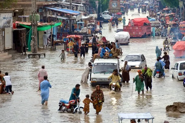 Commuters wade through a flooded street after heavy monsoon rains in Jaffarabad district of Balochistan province on July 27, 2023. Hundreds of people were displaced when at least 50 villages were inundated after the Chenab River burst its banks in Pakistan's Punjab province, officials said on July 27. (Photo by Fida Hussain/AFP Photo)