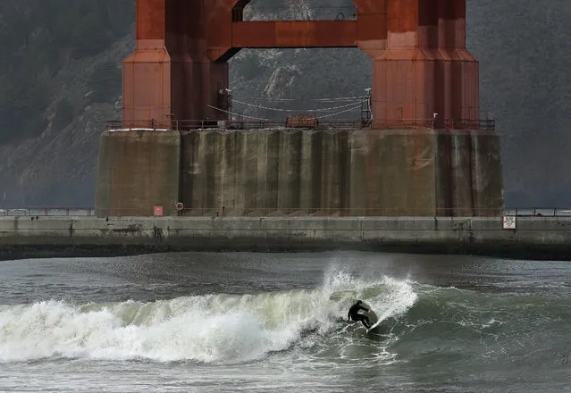 A surfer rides a wave, churned by a winter storm, breaking underneath the south tower of the Golden Gate Bridge, Wednesday, January 6, 2016, in San Francisco Bay. El Nino storms lined up in the Pacific promise to drench parts of the West for more than two weeks and increase fears of mudslides and flash floods in regions stripped bare by wildfires. (Photo by Ben Margot/AP Photo)