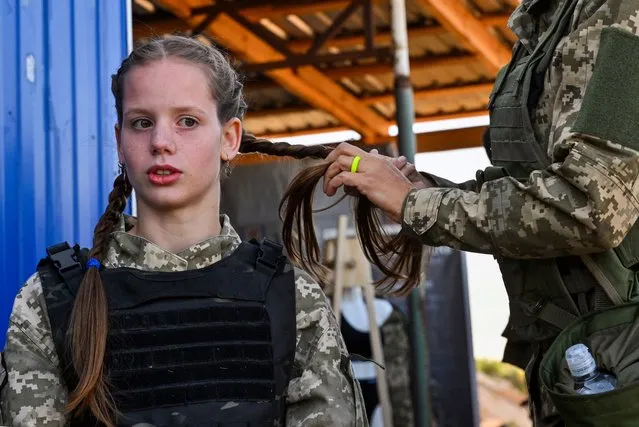 A female Ukrainian cadet, wearing new military uniforms designed specially for women, has her hair braided as he takes part in a training during the "Uniform matters" event organised to present the outfit and test it under military training conditions, on the outskirts of Kyiv on July 12, 2023. (Photo by Sergei Supinsky/AFP Photo)