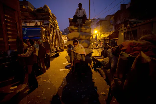 A cart puller carries goods at night in New Delhi, India on Wednesday, November 26, 2014. Thousands of people come to Delhi every year to work odd jobs like pulling carts, then go back home to help their families' small farms at harvest time. (Photo by Saurabh Das/AP Photo)