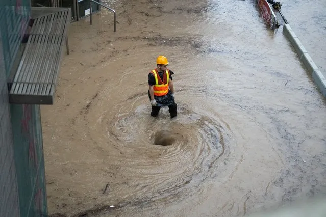 A worker works by a whirlpool as flood waters is drained on a road in Hong Kong on September 8, 2023. Record rainfall in Hong Kong caused widespread flooding in the early hours on September 8, disrupting road and rail traffic just days after the city dodged major damage from a super typhoon. (Photo by Bertha Wang/AFP Photo)