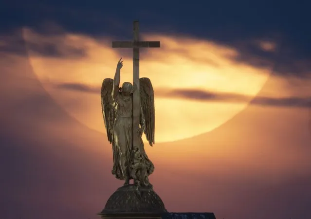 The full moon rises in the clouds over a statue of an angel fixed atop the Alexander Column at the Palace Square in St. Petersburg, Russia, Wednesday, May 26, 2021. (Photo by Dmitri Lovetsky/AP Photo)
