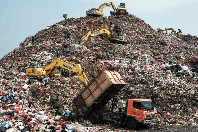 This picture taken on September 14, 2023 shows a truck unloading waste as cranes move waste up to a higher level at the Bantar Gebang landfill, which is the size of 200 football pitches and receives 7,500 tonnes of waste from Jakarta every day, in Bekasi, on the outskirts of Jakarta. Home to around 30 million people, the sprawling megalopolis of Jakarta is facing a trash crisis with its main Bantar Gebang dump site, one of the world's biggest, close to capacity. (Photo by Yasuyoshi Chiba/AFP Photo)