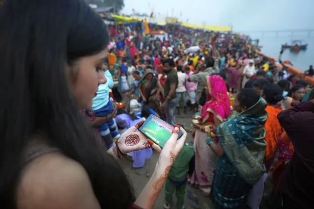 A girl watches the Cricket World Cup final match between Australia and India on a mobile as she joins devotees performing rituals on the banks of river Yamuna during Hindu festival Chhath Puja in Prayagraj, India, Sunday, November 19, 2023. (Photo by Rajesh Kumar Singh/AP Photo)
