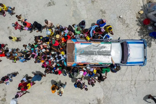 People gather around a car where volunteers distribute food to refugees at a shelter for families displaced by gang violence at the Saint Yves Church in Port-au-Prince, Haiti July 26, 2021. Violence has spiked in Haiti's capital as rival groups battle with one another or the police for control of the streets, displacing thousands and worsening the country's humanitarian crisis. (Photo by Ricardo Arduengo/Reuters)
