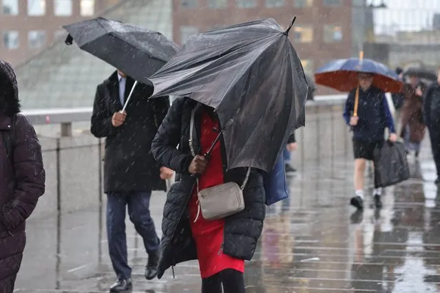 Commuters attempt to shelter as they cross London Bridge during wet and windy weather in Central London on November 1, 2023. Yellow weather warnings for wind and rain are in place for parts of England as Storm Ciarán begins to influence weather in the United Kingdom. (Photo by George Cracknell Wright)