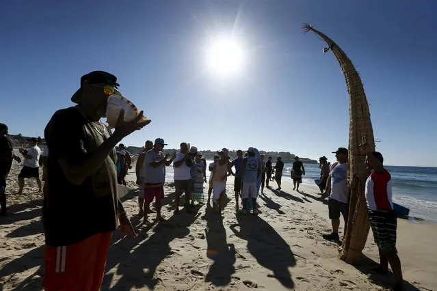 Peruvian surfer Carlos “Huevito” Areola (R) poses alongside his reed board, or “caballito” (little horse), as a man plays a shell (L) in celebration of Huevito's first surf at Sydney's Bondi Beach, February 24, 2016. (Photo by Jason Reed/Reuters)