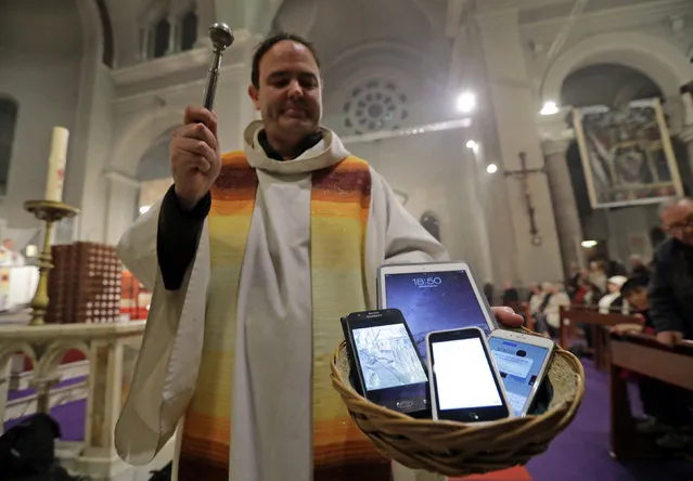 Father Yves Marie Lequin blesses mobile phones and tablets during a mass to honor Saint Francis De Sales, patron Saint of journalists, transmissions and communications at Saint Pierre D'Arene church in Nice, France, January 21, 2017. (Photo by Eric Gaillard/Reuters)