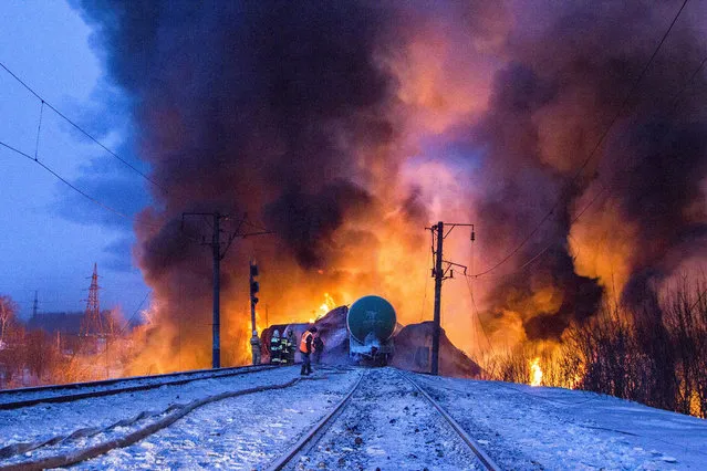 In this photo provided by the Ministry of Emergency Situations Kirov Branch press service, firefighters and emergency ministry employees watch burning tankers early Wednesday, February 5, 2014, near Posdino in Kirov region of Russia, some 800 km (about 500 miles) northeast of Moscow. 32 tankers were derailed and 12 of them burned. No casualties were reported. (Photo by AP Photo/Ministry of Emergency Situations/Kirov Branch Press Service)