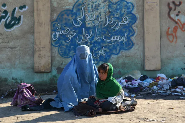 An Afghan woman sits with a girl begging for money, in front of a wall with a Persian sentence that reads,“Child is life, do not exchange her/him with money”, in Mazar-i Sharif, northern of Kabul, Afghanistan, Sunday, January 31, 2016. (Photo by Shiwa Kiyanosh/AP Photo)