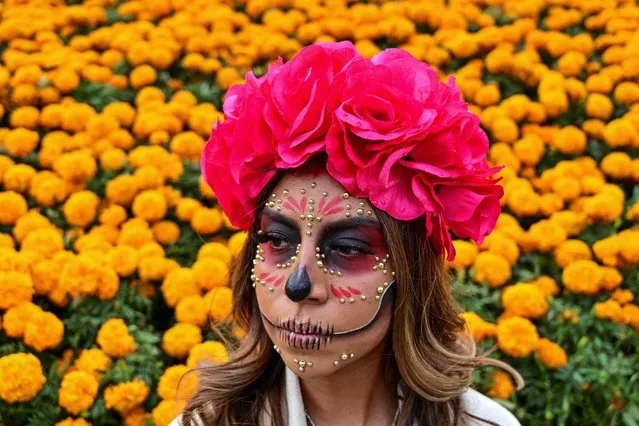 A woman disguised as Catrina poses for a picture in front of decorations with Cempazuchitl -Mexican Marigold (Tagetes erecta)- set along the Paseo de la Reforma avenue within preparations for the Day of the Dead celebration, in Mexico City, on October 21, 2021. (Photo by Pedro Pardo/AFP Photo)