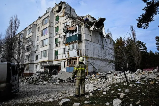 A rescuer looks at a residential building damaged by a missile attack in the village of Kluhyno-Bashkyrivka, Kharkiv region on December 2, 2022, amid the Russian invasion of Ukraine. (Photo by Sergey Bobok/AFP Photo)