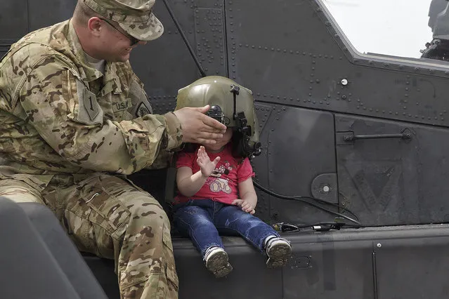 A US serviceman holds a pilot helmet for child posing on an Apache attack helicopter in Ploiesti, Romania, Wednesday, May 13, 2015. (Photo by Vadim Ghirda/AP Photo)